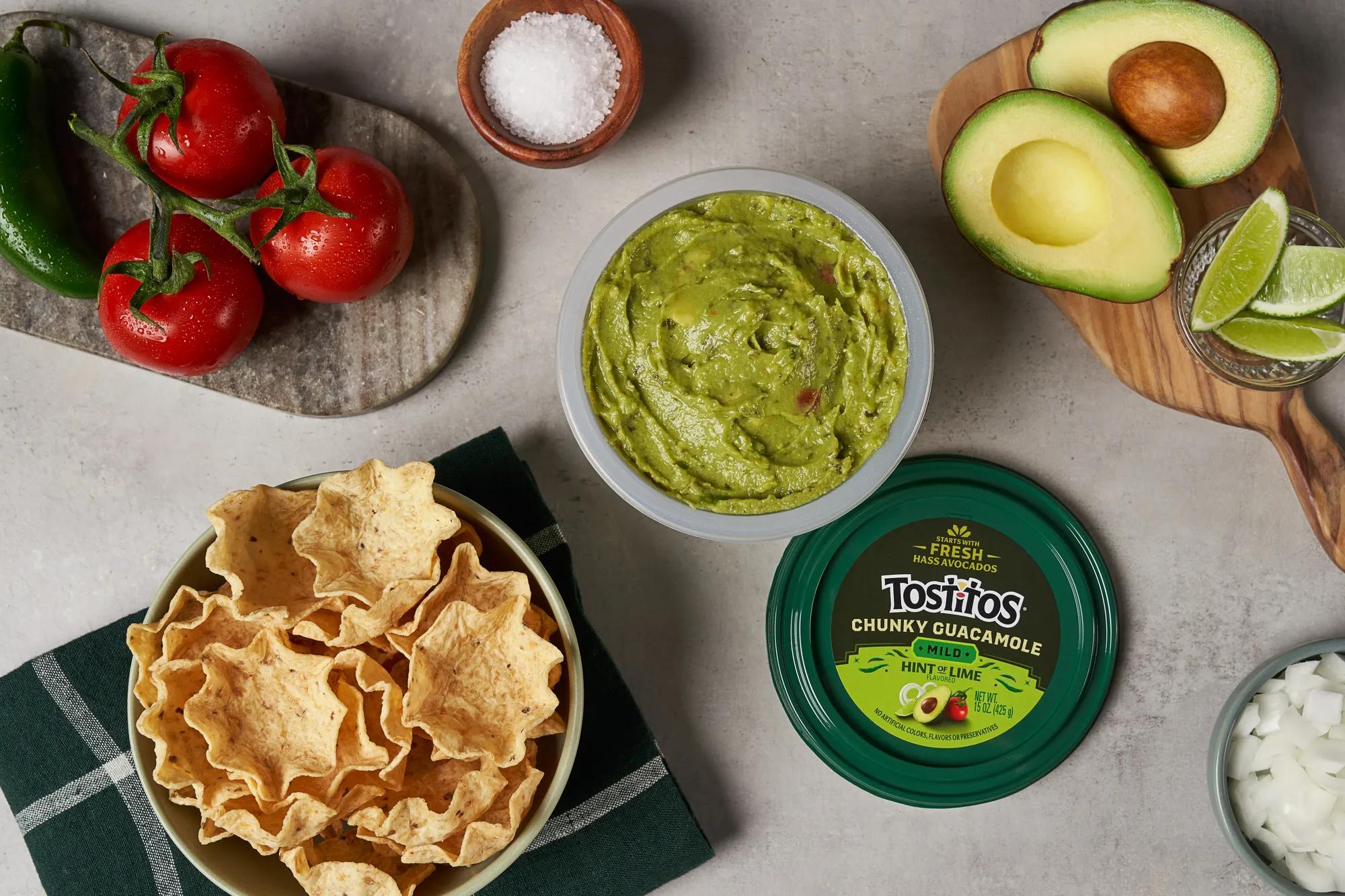 New refrigerated Tostitos® Chunky Guacamole: Mild, Hint of Lime Flavored Dip 15 oz. tub, surrounded by fresh ingredients and Tostitos® SCOOPS!® Original in refreshed packaging. Photo credit: Brielle Patton.
